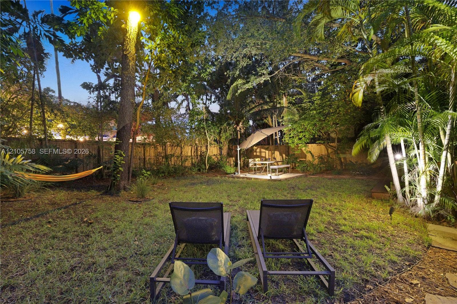 668 NE 70th Street, Miami, FL 33138 Private backyard featuring a fenced perimeter, mature trees, lush tropical landscaping, and a paved patio area