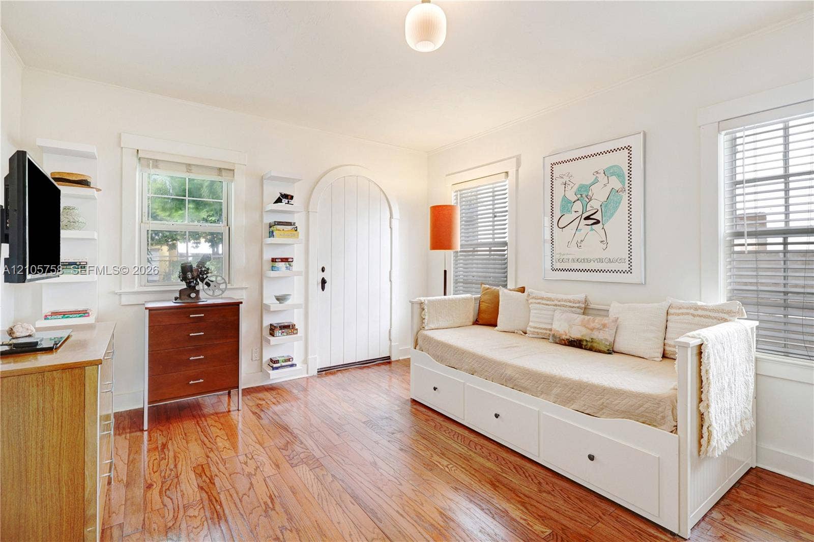 668 NE 70th Street, Miami, FL 33138 Arched solid-panel door featuring wood-finish flooring, built-in shelving units, and horizontal window blinds