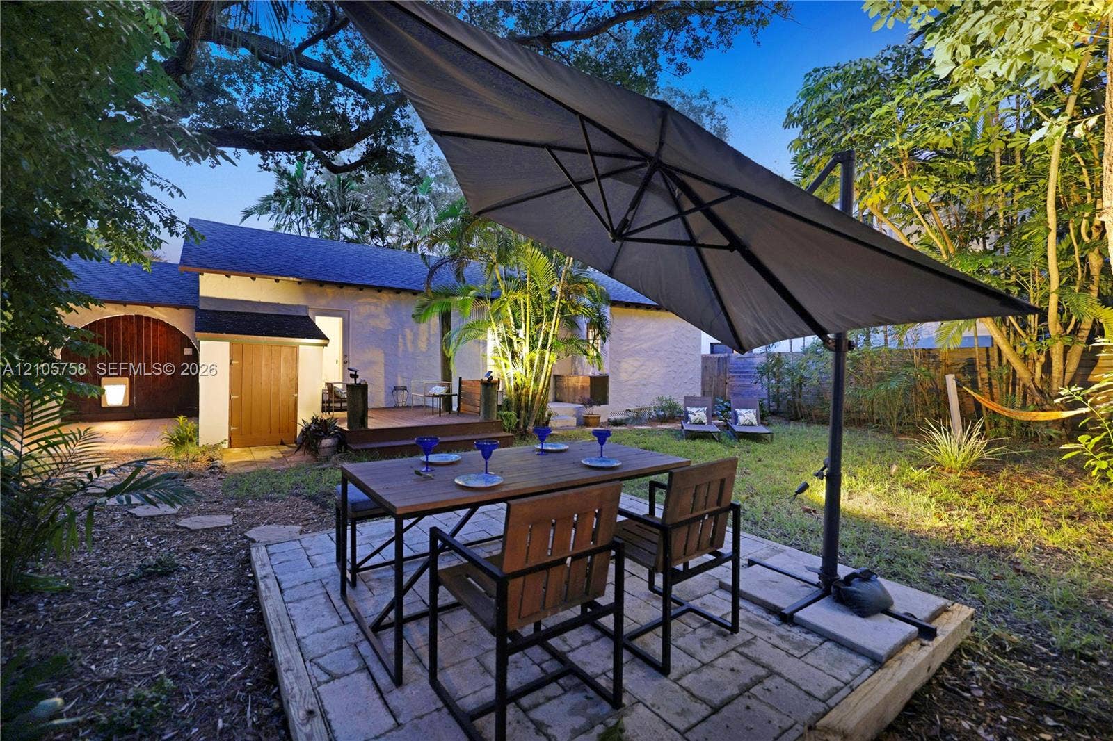 668 NE 70th Street, Miami, FL 33138 Backyard featuring a paved stone patio, raised wooden deck, mature trees, and landscaping