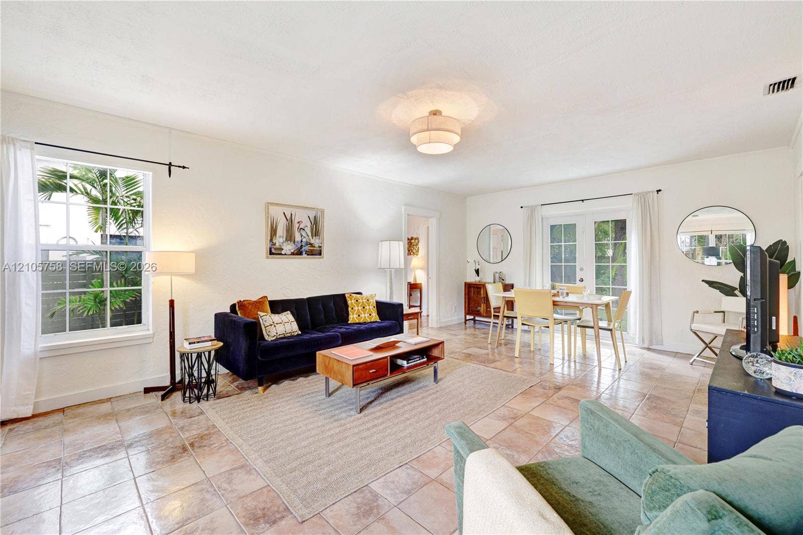 668 NE 70th Street, Miami, FL 33138 Open living area featuring large-format stone tile flooring, multi-pane windows, a central tiered flush-mount light fixture, and French doors