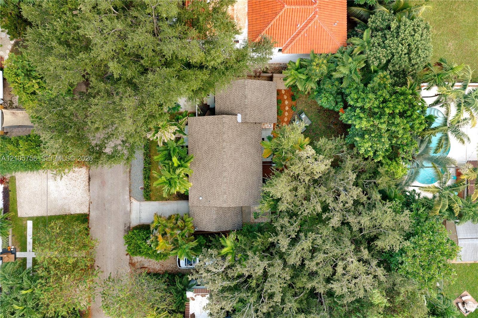 668 NE 70th Street, Miami, FL 33138 Aerial perspective of property featuring shingled roofing, paved driveway, mature canopy trees, and an in-ground swimming pool