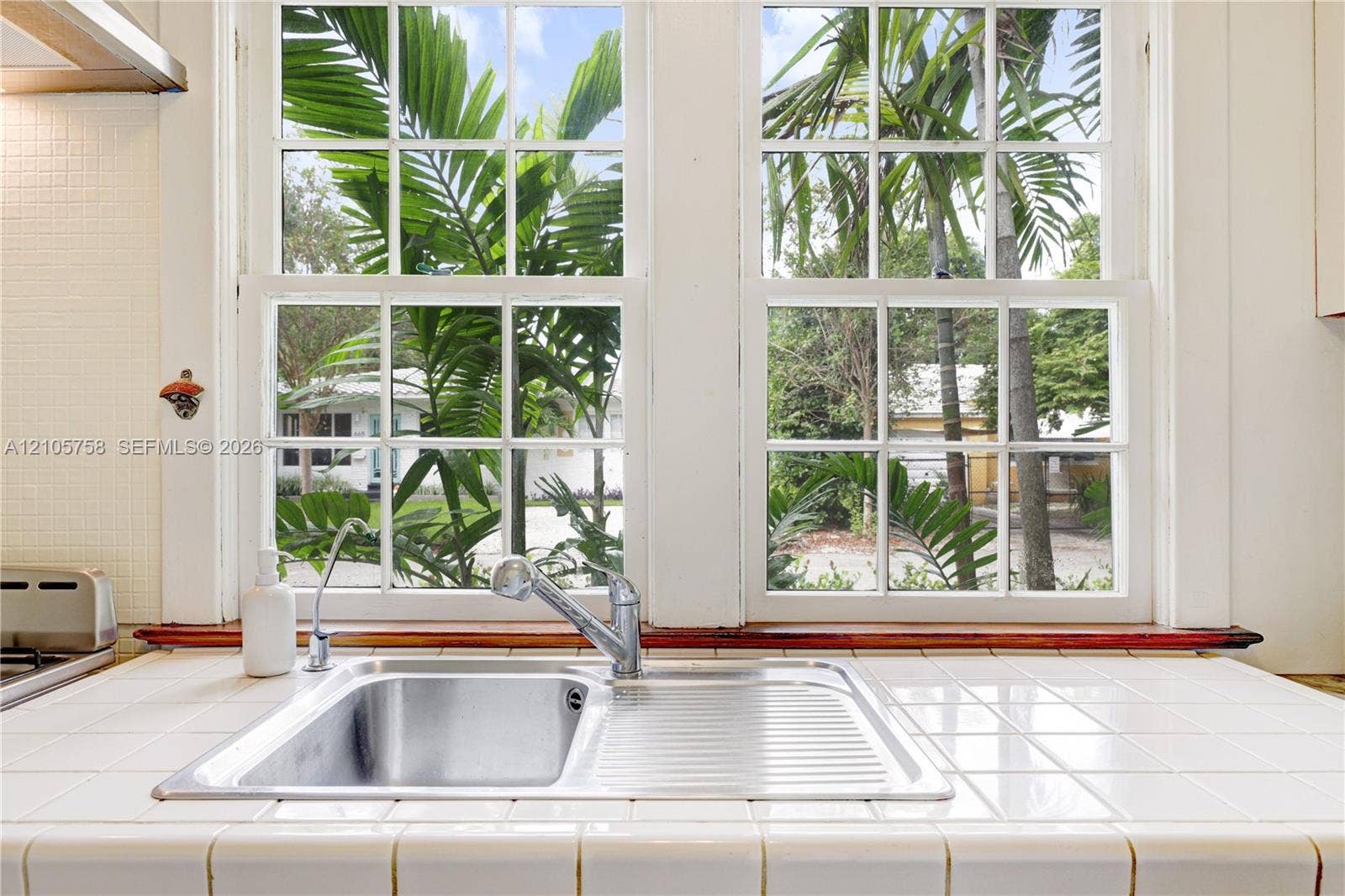 668 NE 70th Street, Miami, FL 33138 Double-basin stainless steel sink with a high-arch pull-down faucet, white tile countertop, and multi-pane double-hung windows