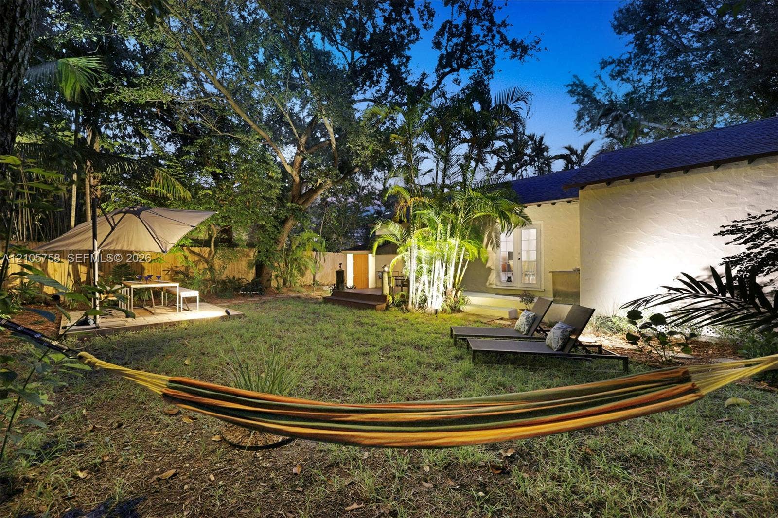 668 NE 70th Street, Miami, FL 33138 Private backyard featuring a manicured lawn, wood-finish decking, mature trees, and high-contrast exterior wall masonry