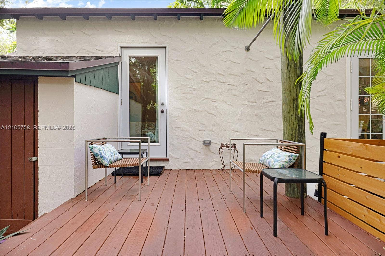 668 NE 70th Street, Miami, FL 33138 Textured stucco exterior featuring a wood-tone deck, horizontal wood-slat privacy fencing, and a paneled wood-finish access door