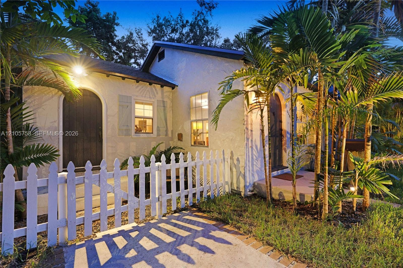 668 NE 70th Street, Miami, FL 33138 Stucco exterior featuring an arched entry, wood-finish shutters, a covered porch, and a picket fence