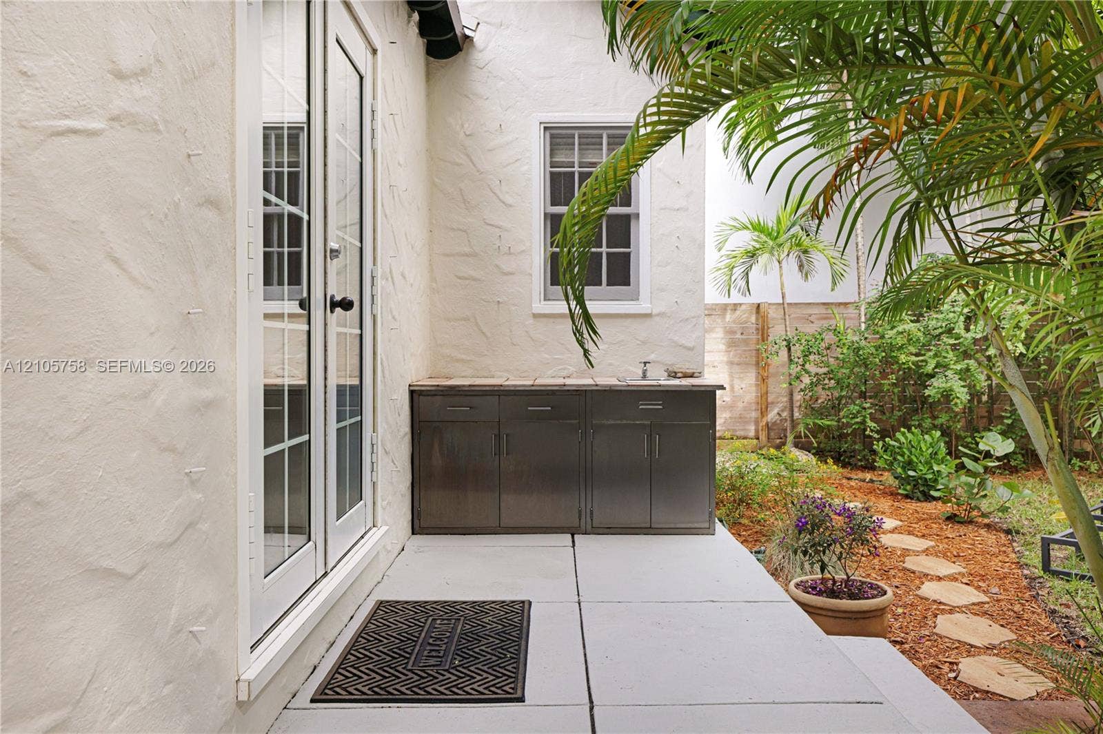 668 NE 70th Street, Miami, FL 33138 Outdoor living area featuring a paved patio, built-in stainless steel cabinetry with a stone countertop and sink, double-paned French doors, and landscaping with a stone path