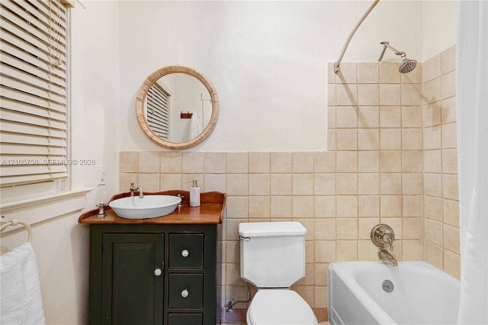 668 NE 70th Street, Miami, FL 33138 Bathroom featuring a dark-finish vanity, vessel sink, round wall-mounted mirror, and square-tile tub surround