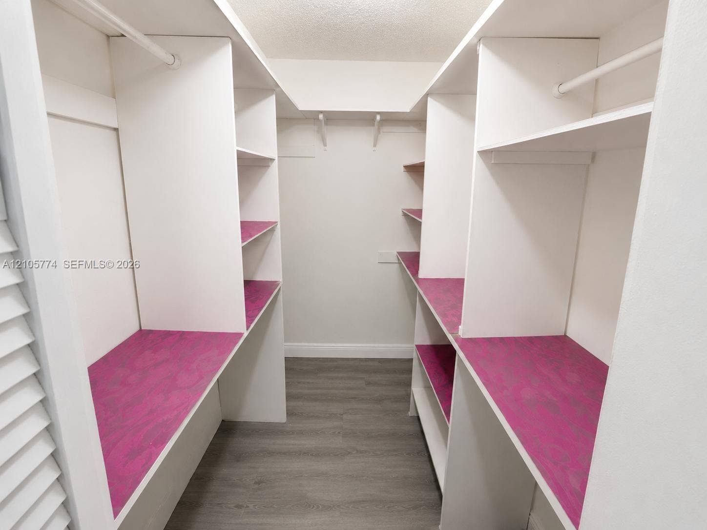 10343 Greenhouse Road, Pembroke Pines, FL 33026 Walk-in closet featuring white built-in shelving, integrated garment rods, vibrant magenta laminate surfaces, and wood-finish flooring