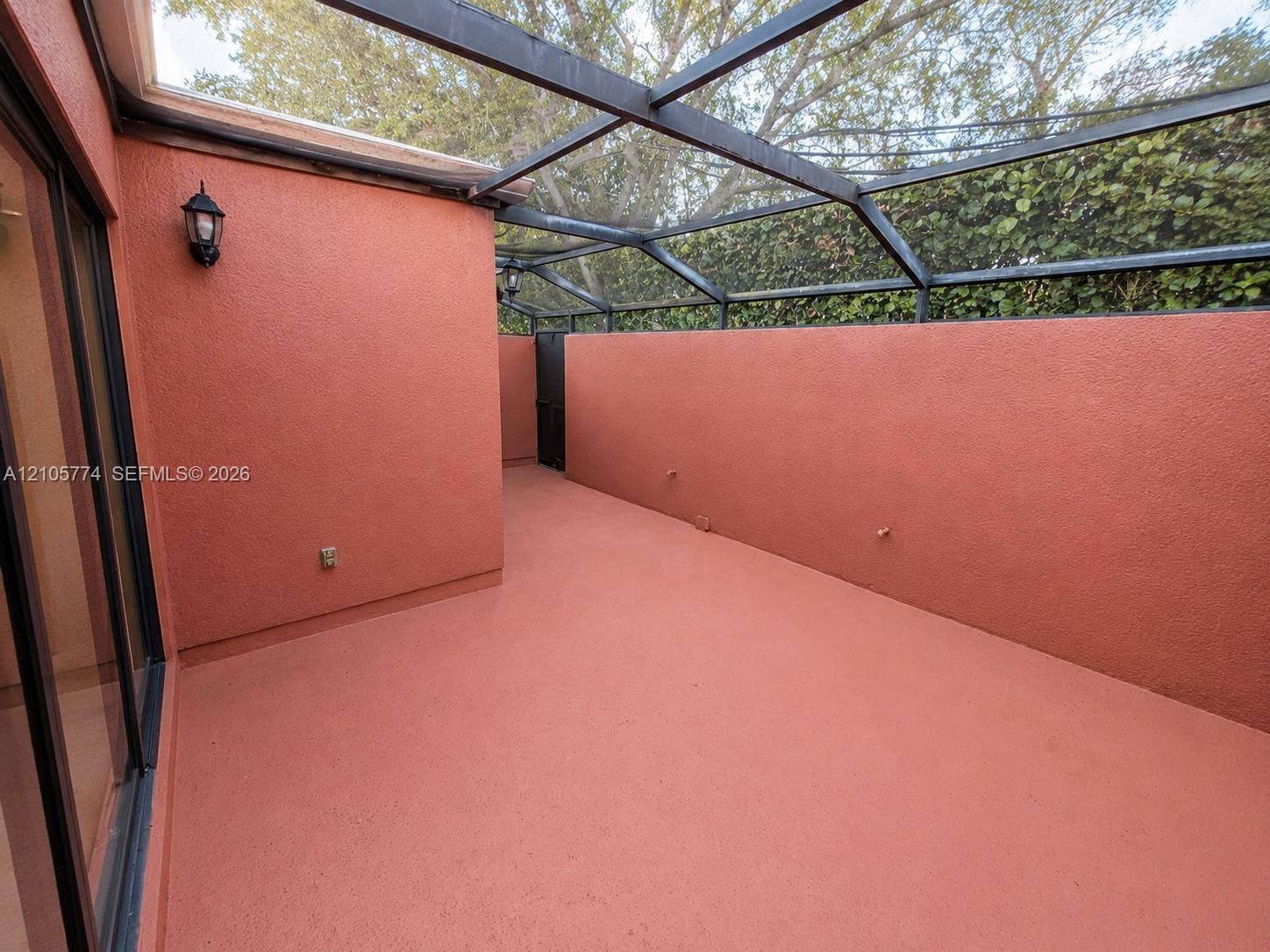 10343 Greenhouse Road, Pembroke Pines, FL 33026 Enclosed patio featuring a screen roof, textured masonry walls, painted concrete flooring, and wall-mounted exterior lighting
