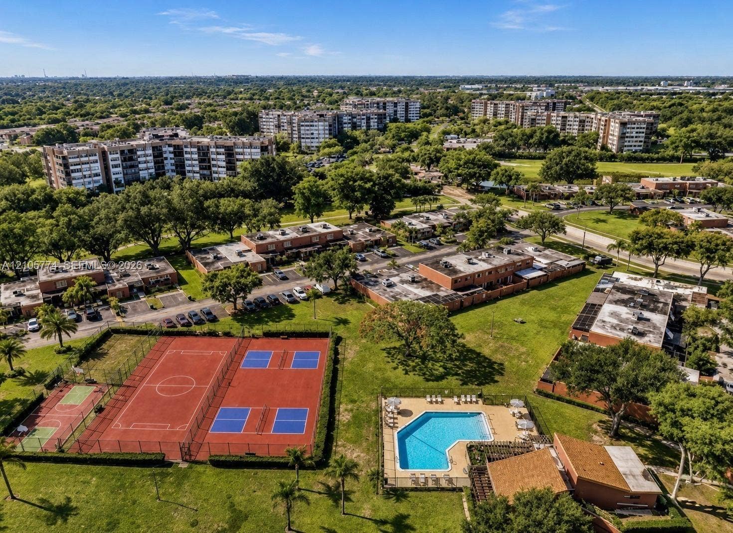 10343 Greenhouse Road, Pembroke Pines, FL 33026 Aerial perspective of the property featuring a fenced swimming pool, multi-use sports courts, expansive manicured grounds, and mature tree canopy