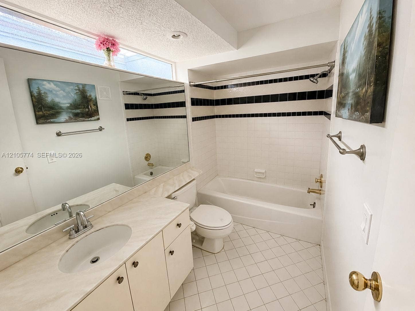 10343 Greenhouse Road, Pembroke Pines, FL 33026 Bathroom featuring a single-sink vanity with a solid-surface countertop, full-width wall mirror, transom window, and a bathtub with decorative tile surround