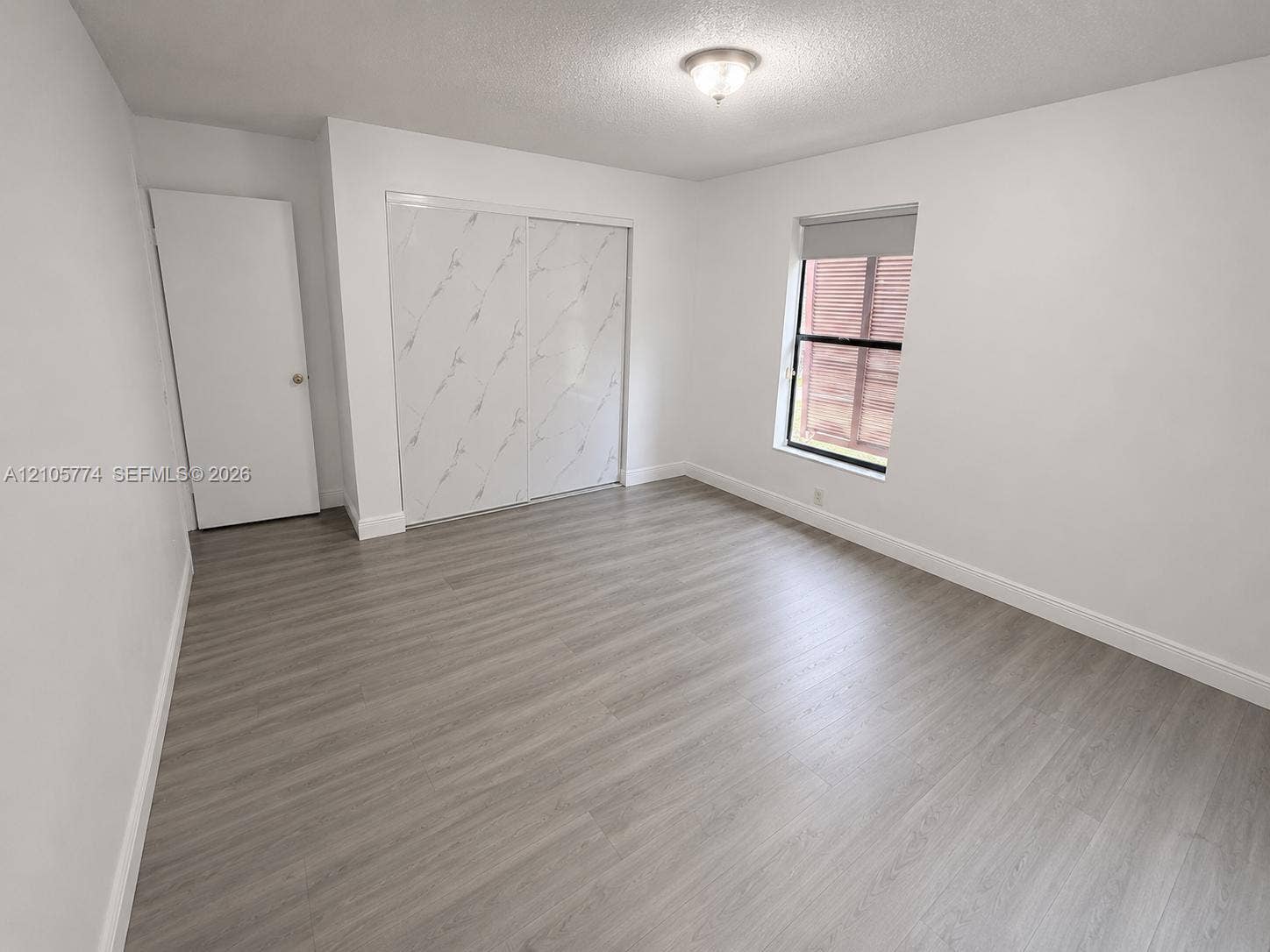 10343 Greenhouse Road, Pembroke Pines, FL 33026 Interior space featuring wood-finish flooring, sliding closet doors with marble-patterned finish, white walls, and a recessed ceiling light fixture
