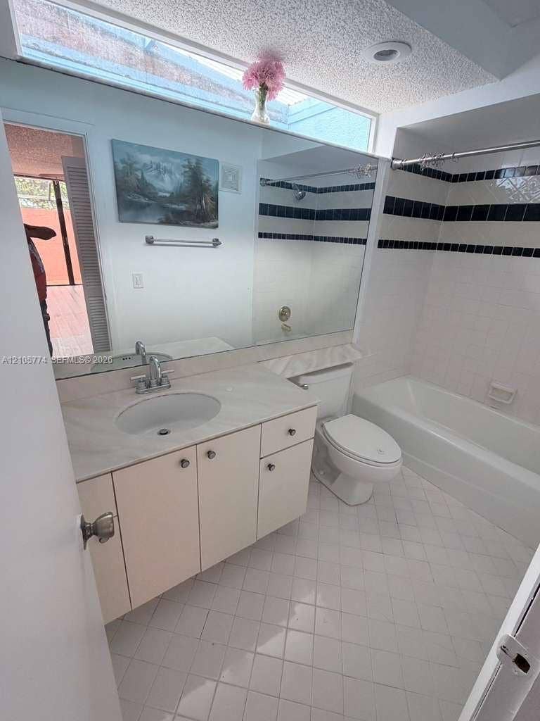 10343 Greenhouse Road, Pembroke Pines, FL 33026 Bathroom featuring a skylight, vanity with an integrated sink and stone-finish countertop, full-width mirror, and a tile-surround bathtub with dual decorative accent bands