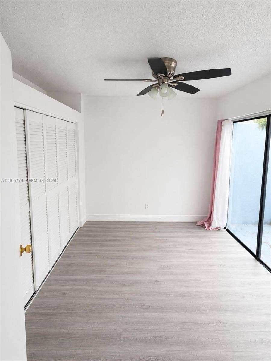 10343 Greenhouse Road, Pembroke Pines, FL 33026 Neutral-toned wood-finish flooring, floor-to-ceiling sliding glass door, multi-panel louvered closet doors, and a ceiling fan with integrated lighting