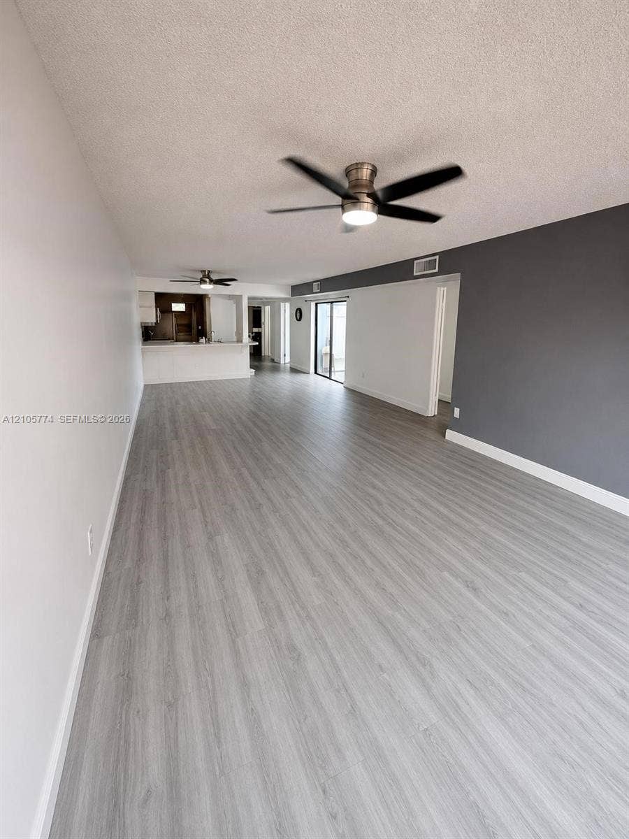 10343 Greenhouse Road, Pembroke Pines, FL 33026 Open-concept interior featuring wood-finish flooring, two ceiling fans, a contrasting accent wall, and a kitchen breakfast bar