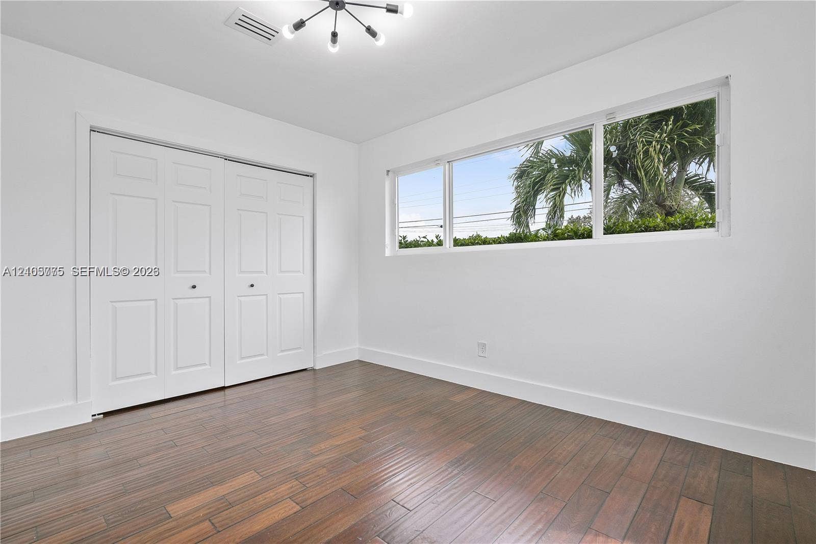 21230 NE 24th Court, Miami, FL 33180 Room featuring dark-toned wood-finish flooring, a multi-arm modern light fixture, expansive horizontal window, and floor-to-ceiling built-in closet with dual paneled doors