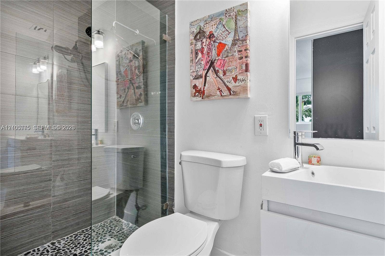 21230 NE 24th Court, Miami, FL 33180 Bathroom featuring a frameless glass walk-in shower with horizontal tile surround and pebble tile flooring, white vanity with a rectangular integrated sink, and polished chrome fixtures
