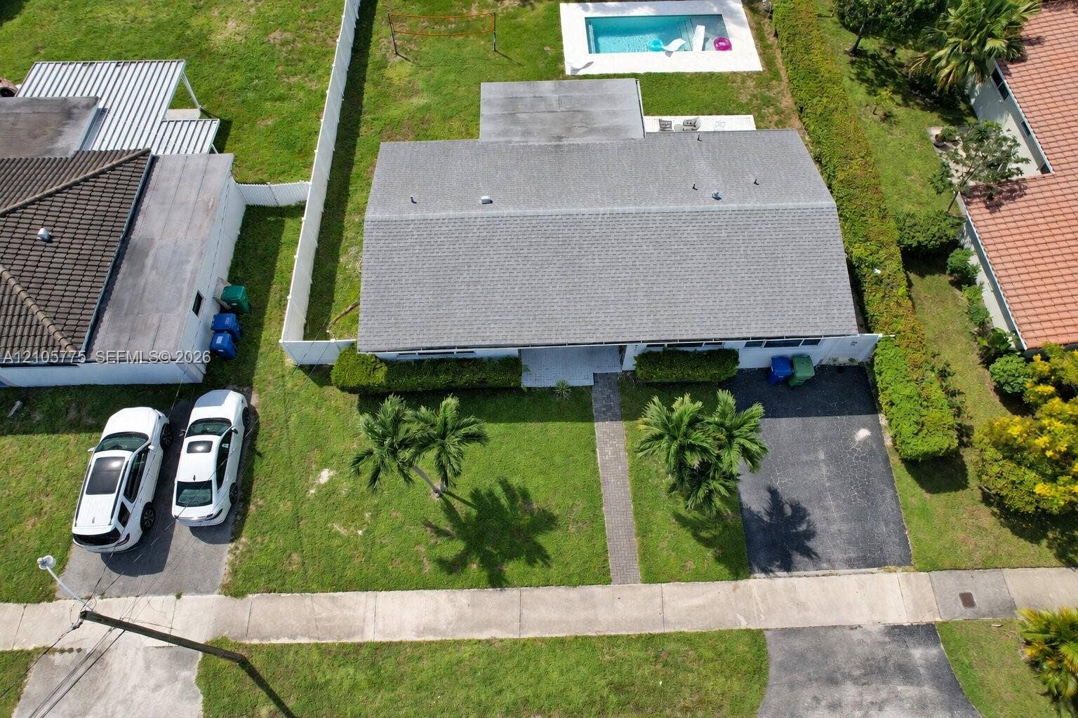 21230 NE 24th Court, Miami, FL 33180 Aerial perspective featuring a shingled roof, rear swimming pool, paved driveway, concrete walkway, and landscaped lawn
