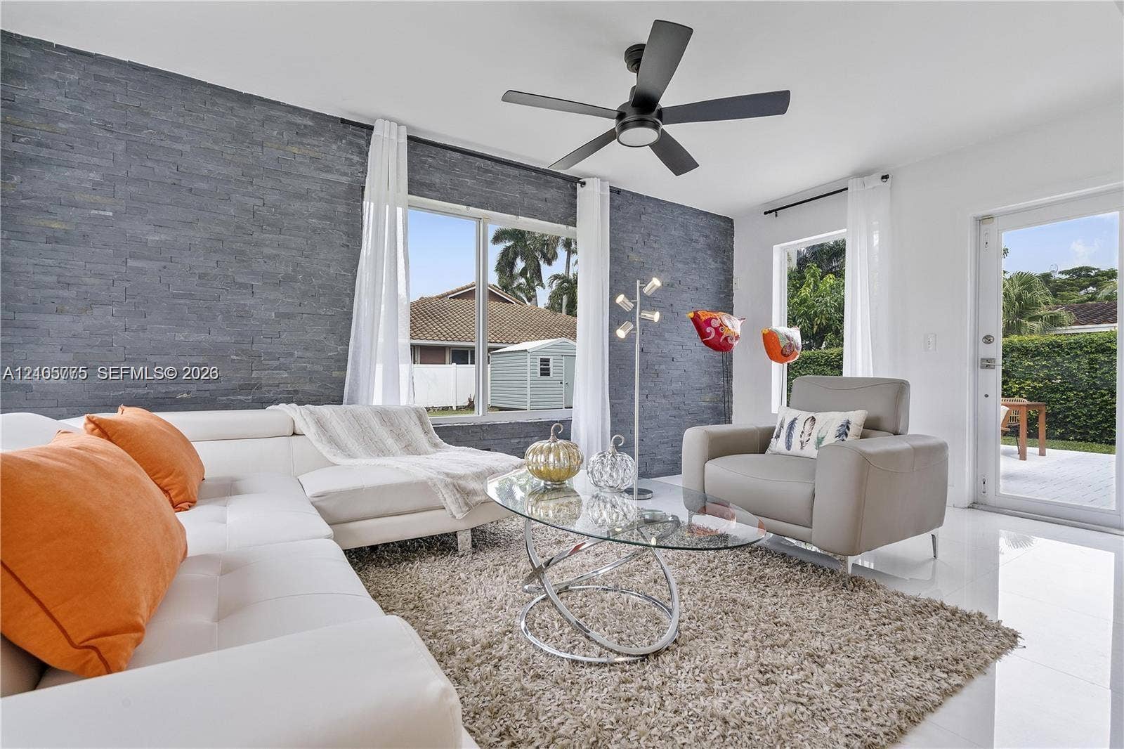 21230 NE 24th Court, Miami, FL 33180 Living area featuring a floor-to-ceiling charcoal stone veneer accent wall, large picture windows, matte black ceiling fan with integrated lighting, and white ceramic tile flooring
