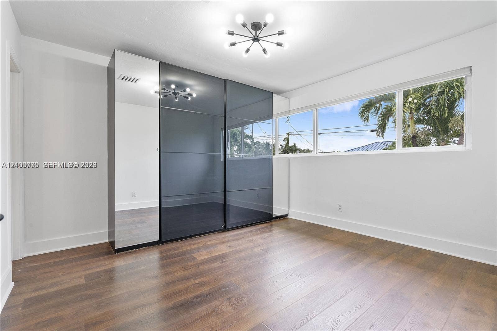 21230 NE 24th Court, Miami, FL 33180 Room featuring wood-finish flooring, large multi-pane horizontal window, modern sputnik-style ceiling light, and full-height built-in wardrobe with mirrored and dark-tinted glass sliding doors