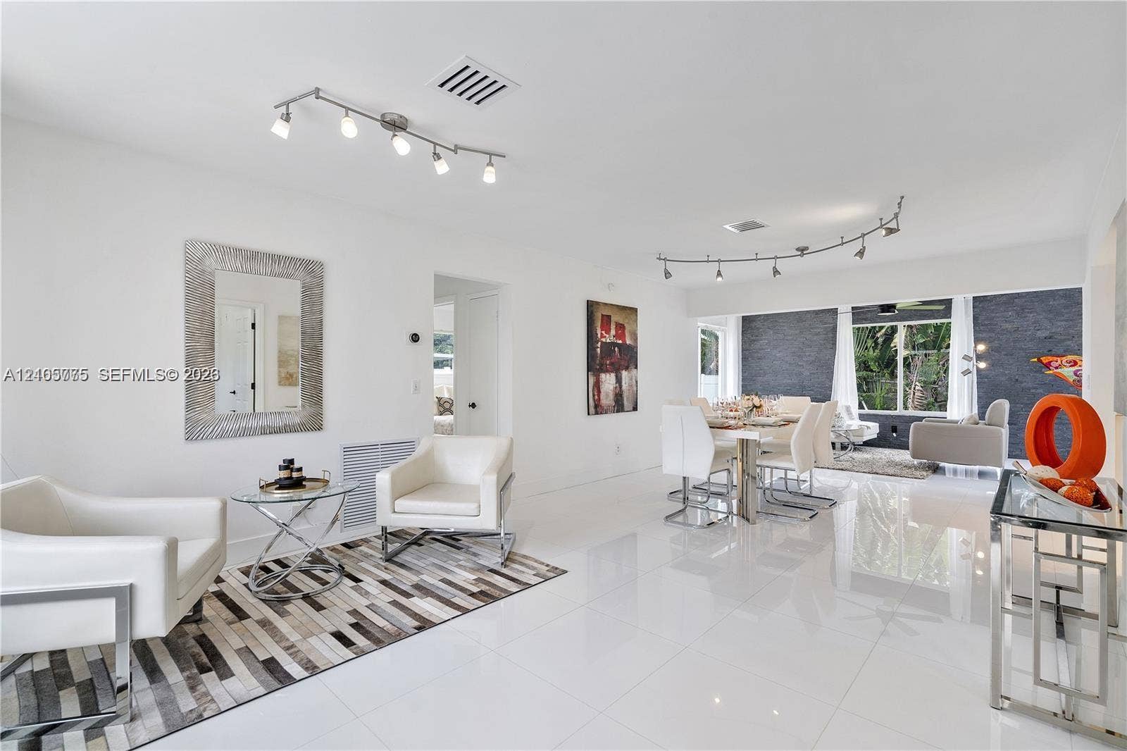 21230 NE 24th Court, Miami, FL 33180 Open-concept interior featuring large-format white tile flooring, track lighting, and a textured charcoal accent wall