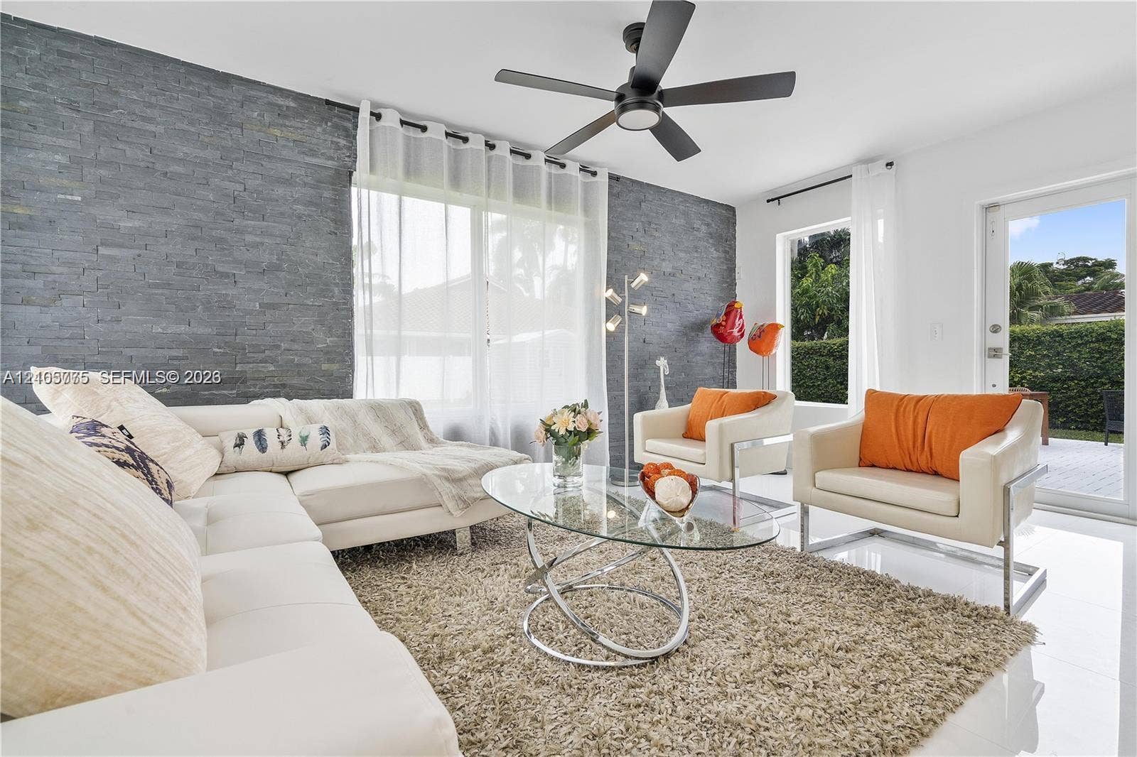 21230 NE 24th Court, Miami, FL 33180 Living space featuring a charcoal-toned stacked stone accent wall, large-format tile flooring, and a modern matte black ceiling fan