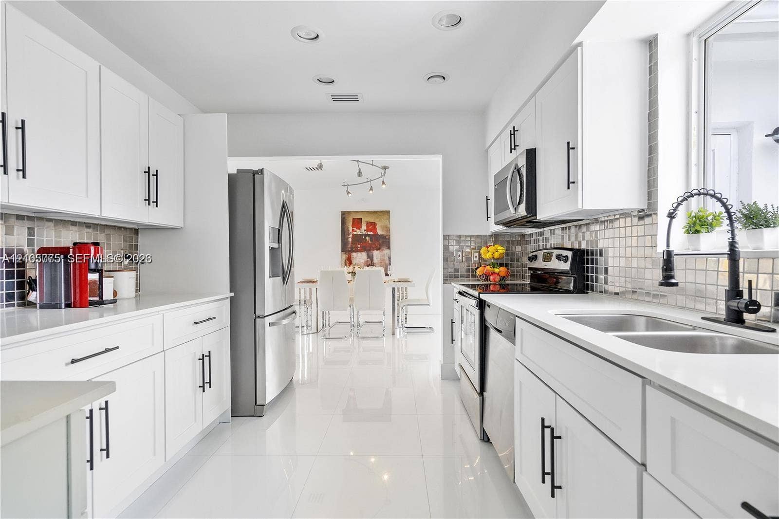 21230 NE 24th Court, Miami, FL 33180 Kitchen featuring white shaker-style cabinetry, stainless steel appliances, tiled backsplash, dual-basin stainless steel sink with a matte black faucet, and polished tile flooring