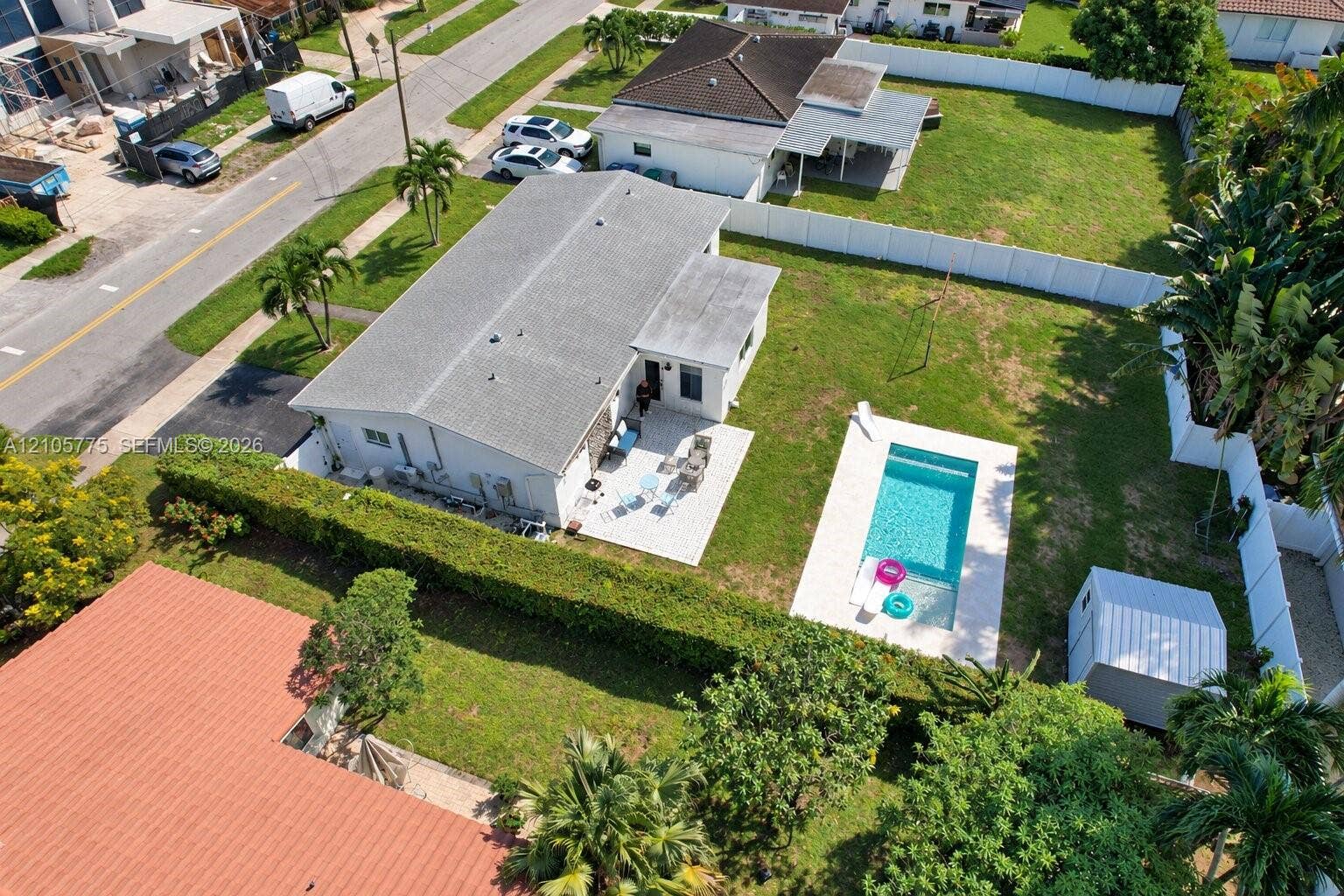 21230 NE 24th Court, Miami, FL 33180 Aerial perspective of a property featuring an in-ground swimming pool, paved patio, expansive lawn, white vinyl perimeter fencing, and a detached storage structure
