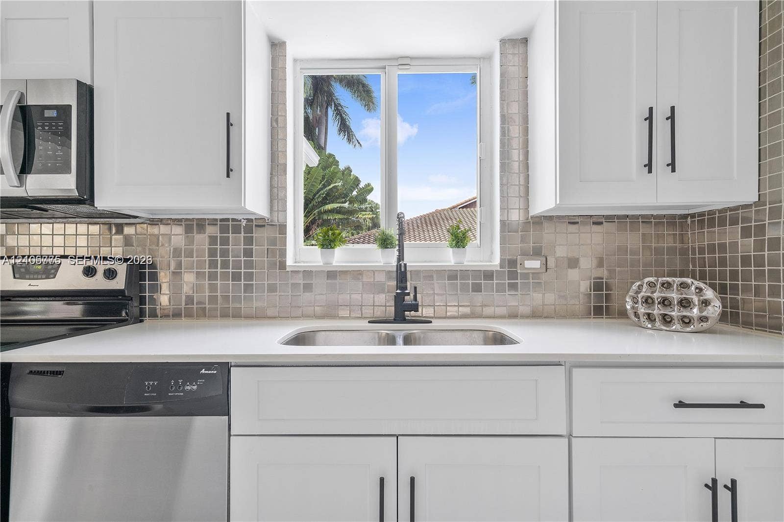 21230 NE 24th Court, Miami, FL 33180 Kitchen featuring white shaker-style cabinetry, matte black hardware, stainless steel appliances, quartz countertops, and a metallic mosaic tile backsplash