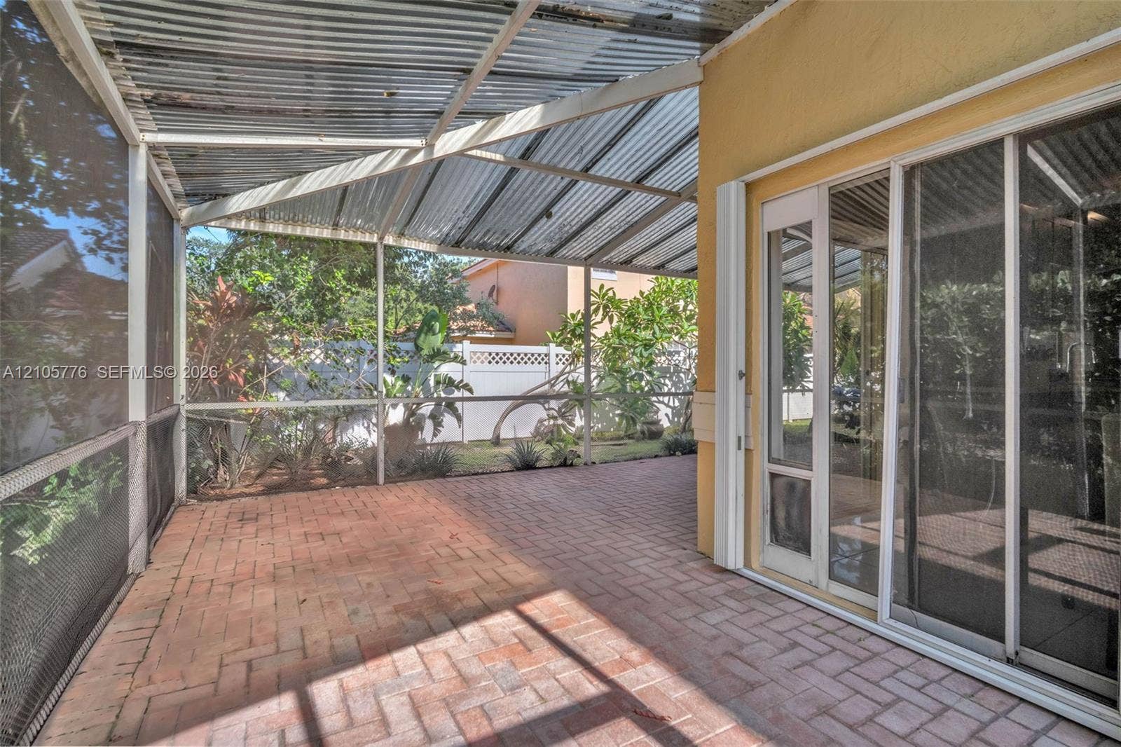 Screened-in patio featuring a corrugated metal roof, brick paver flooring, and sliding glass door access