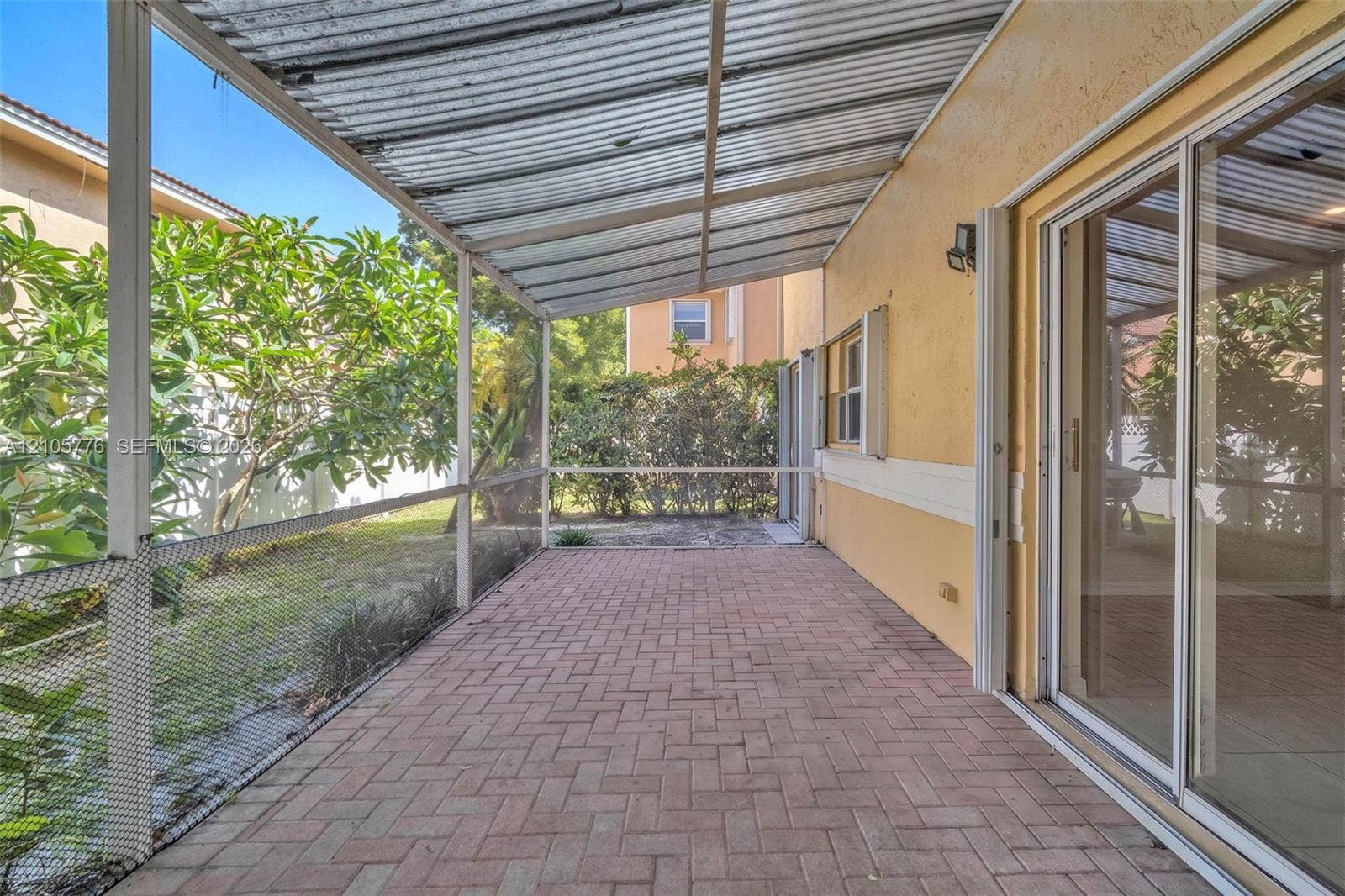 Screened patio featuring a corrugated metal roof, brick paver flooring, sliding glass door entry, and wall-mounted exterior lighting