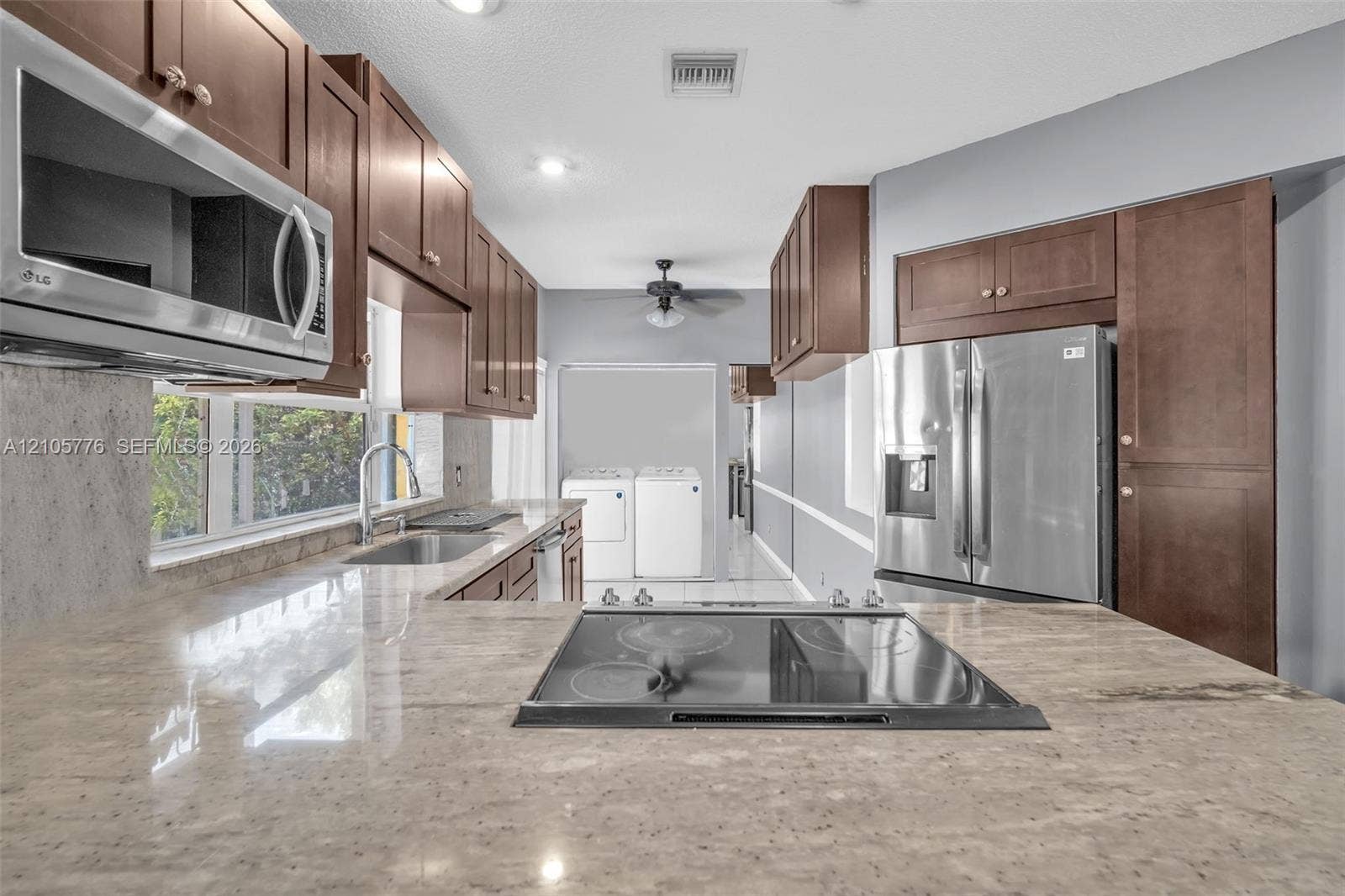 Kitchen featuring stained-wood cabinetry, stone countertops, integrated stainless steel appliances, and a cooktop set within the island