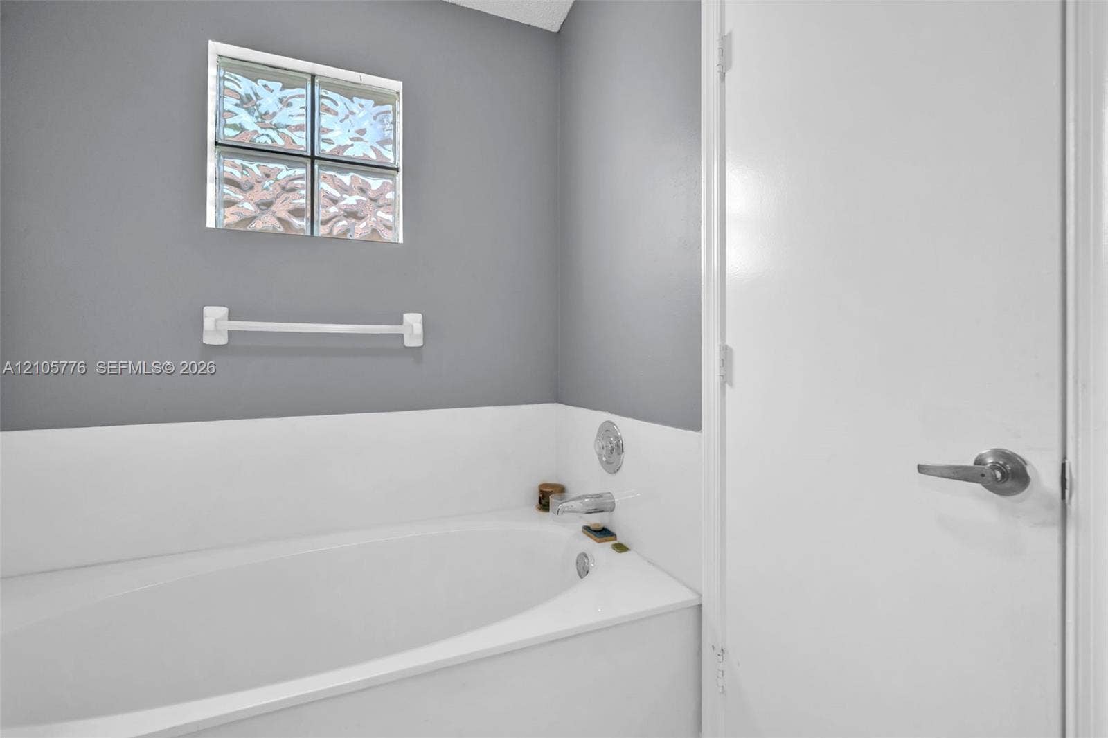 Built-in soaking tub with a white surround, glass block window, chrome faucet fixture, and mounted towel bar