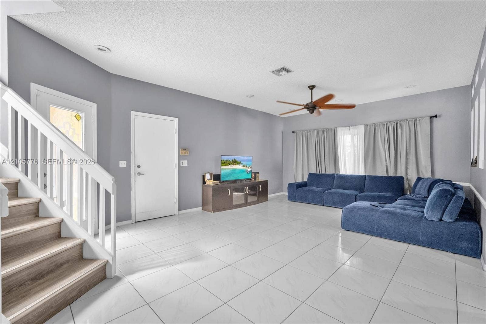 Open-concept interior featuring large-format tile flooring, wood-finish staircase treads, white baluster railings, recessed lighting, and a ceiling fan