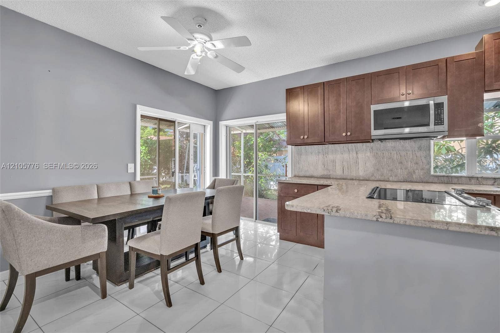 Kitchen featuring wood cabinetry, stone countertops, stone-finish backsplash, tile flooring, and integrated microwave