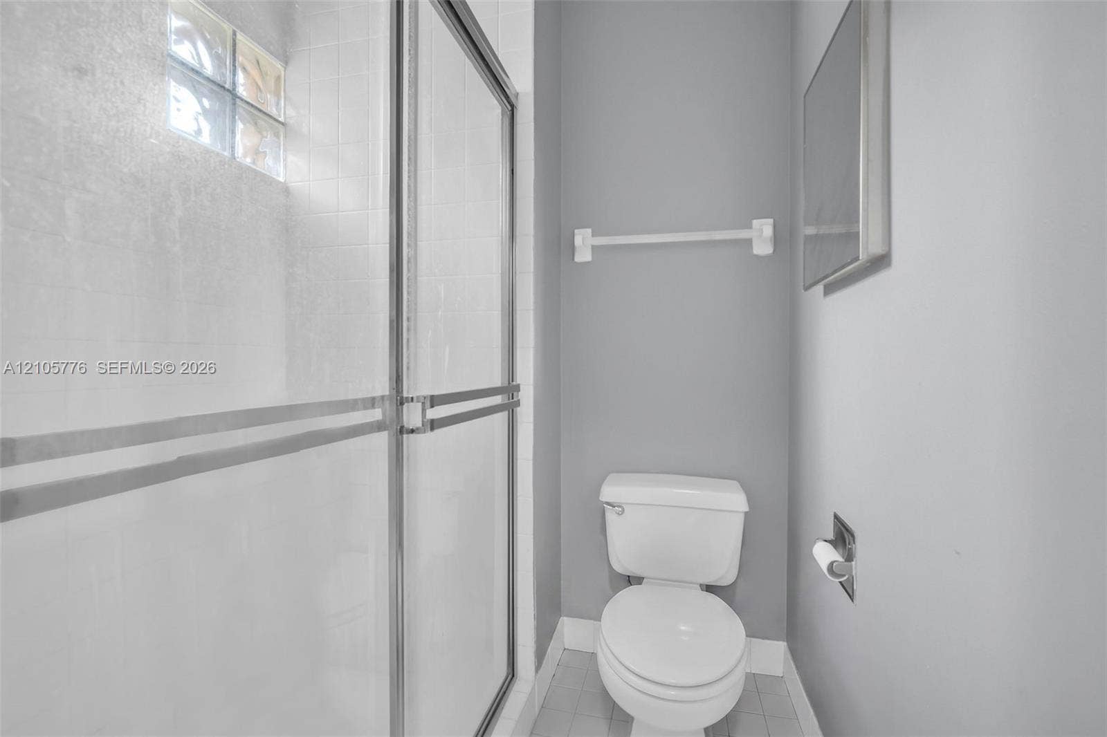 Shower enclosure with glass sliding doors, tiled surround, glass block window, and white porcelain toilet