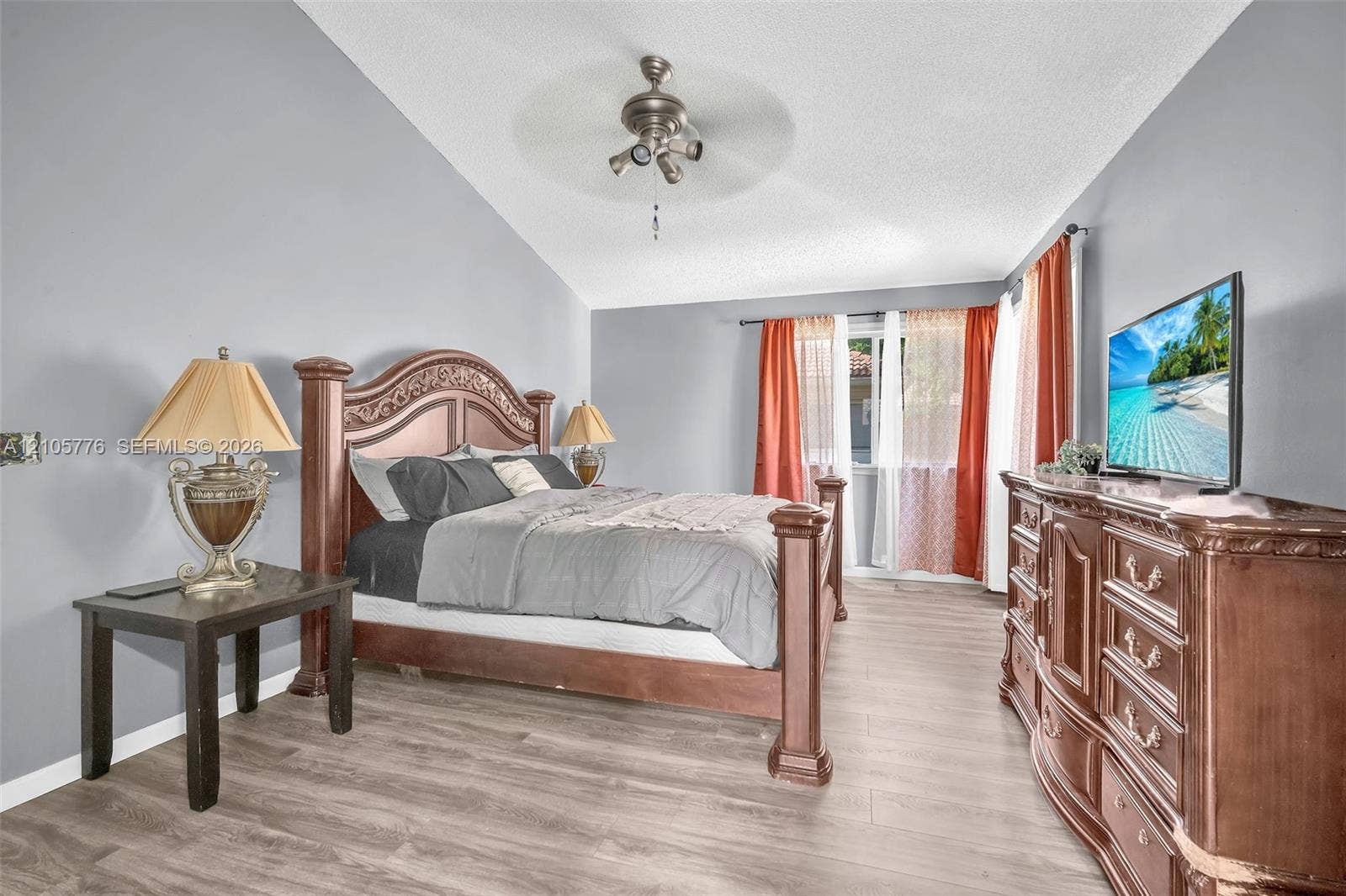 Vaulted ceilings featuring a centrally mounted ceiling fan and light fixture, complemented by neutral wall paint and wood-finish flooring