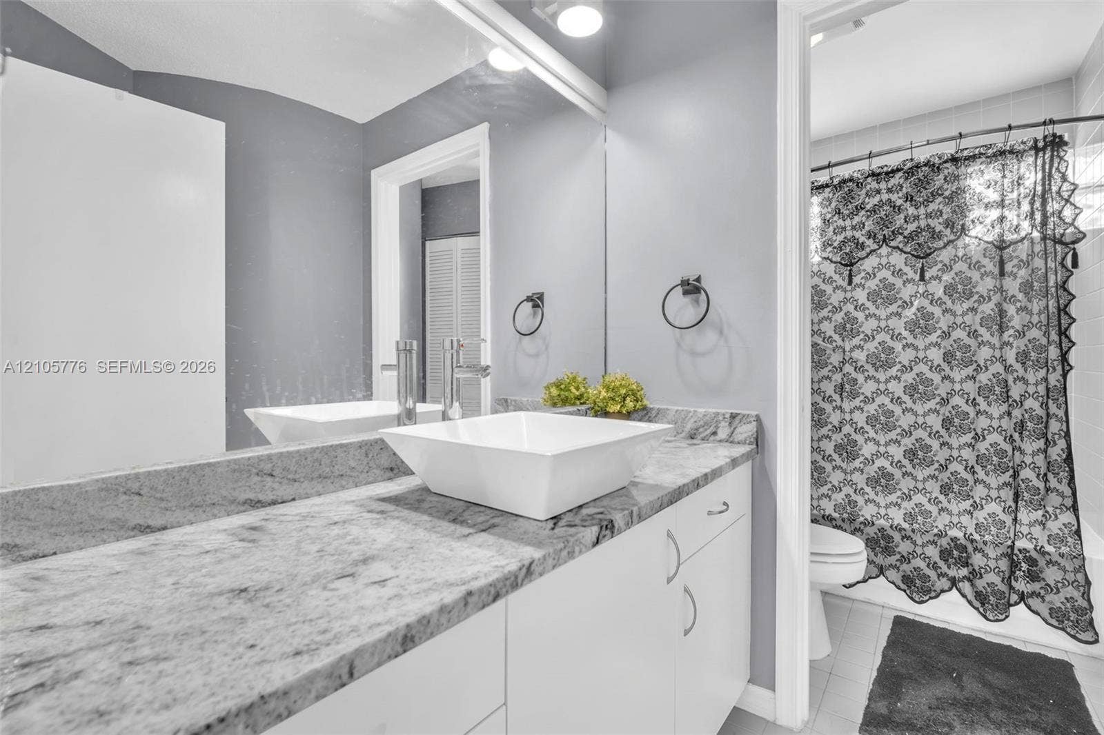 Stone-surface vanity featuring a white vessel sink, polished chrome faucet, full-width wall mirror, and white flat-panel cabinetry