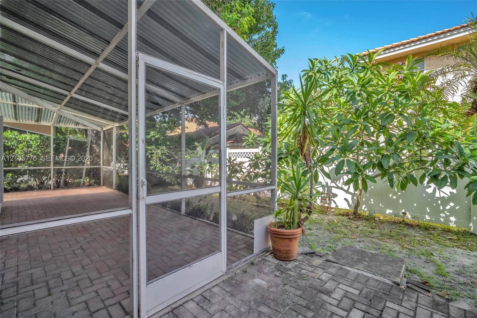 Screened-in patio with a metal roof and herringbone-patterned brick paver flooring, complemented by an outdoor brick paver area and perimeter fencing