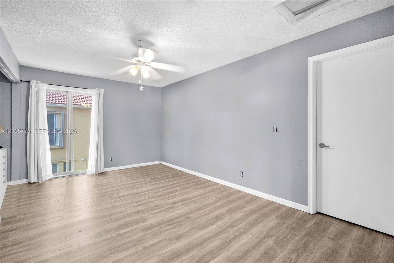 Interior space featuring light-toned wood-finish flooring, neutral wall paint, a ceiling fan with integrated lighting, and a sliding glass door