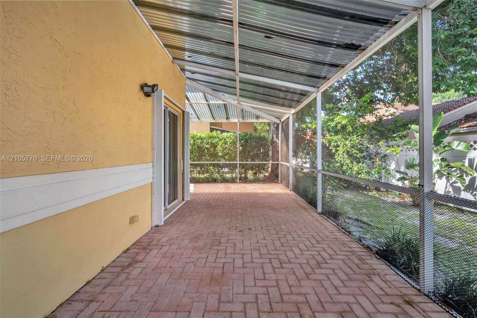 Screened-in patio featuring brick paver flooring, a corrugated metal roof, and an exterior wall-mounted light fixture