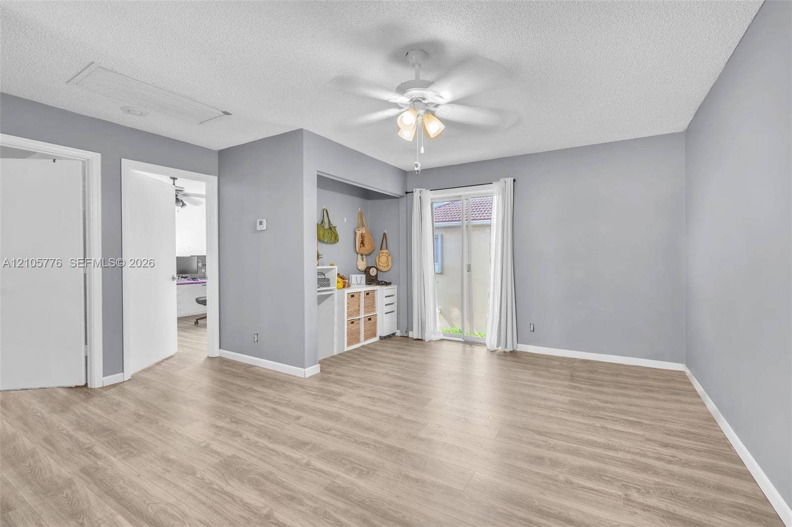 Room with wood-finish flooring, ceiling fan with integrated lighting, and sliding glass door