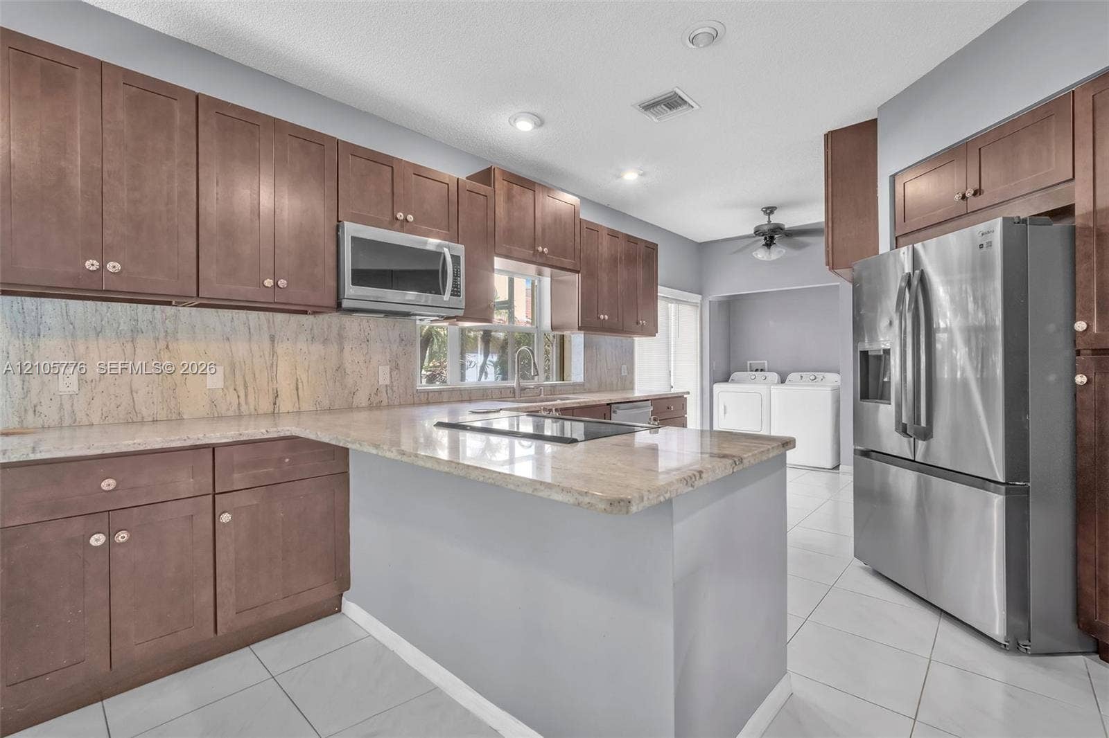 Kitchen featuring dark wood cabinetry, stone-surface countertops, full-height stone backsplash, recessed lighting, and stainless steel appliances
