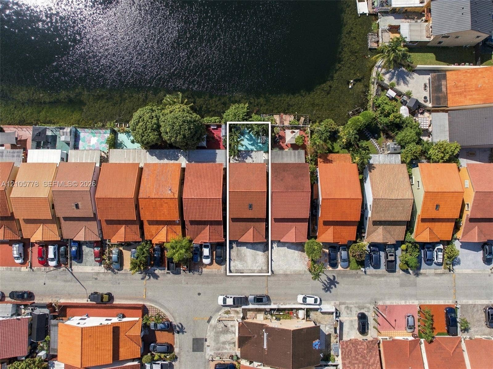 Aerial perspective of a waterfront property featuring a tile roof, concrete driveway, and a private rear pool