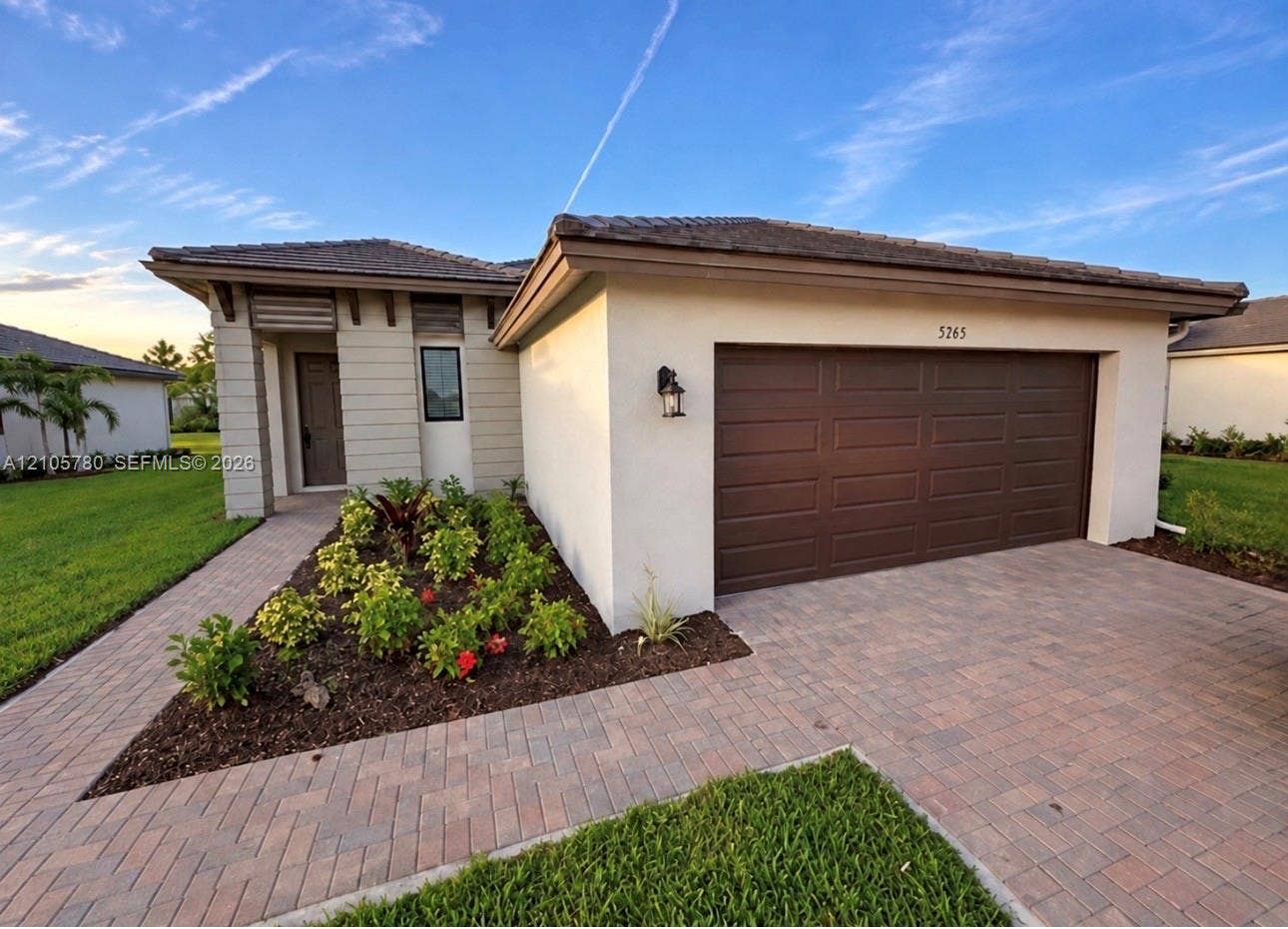 Single-story exterior featuring a tile roof, stucco siding, paver driveway, two-car garage, and a paver walkway leading to the entrance