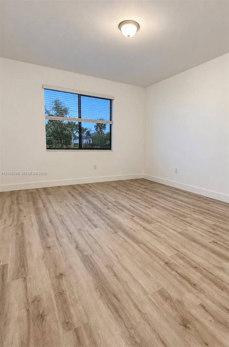 Room featuring neutral wall paint, wood-finish flooring, a single-pane window, and a ceiling-mounted light fixture