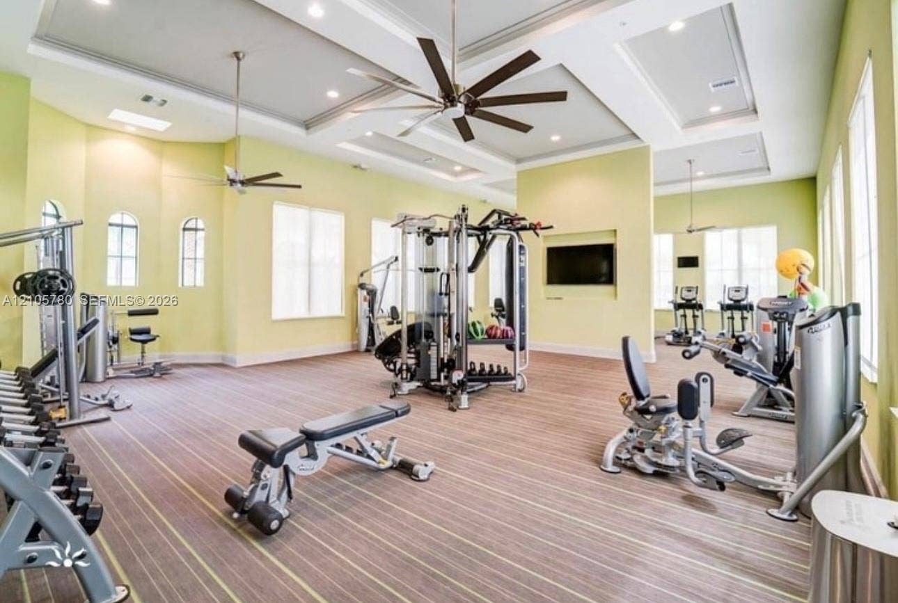 Fitness center featuring a double-tray ceiling, multiple large-blade ceiling fans, inset wall shelving for media, and arched window detailing