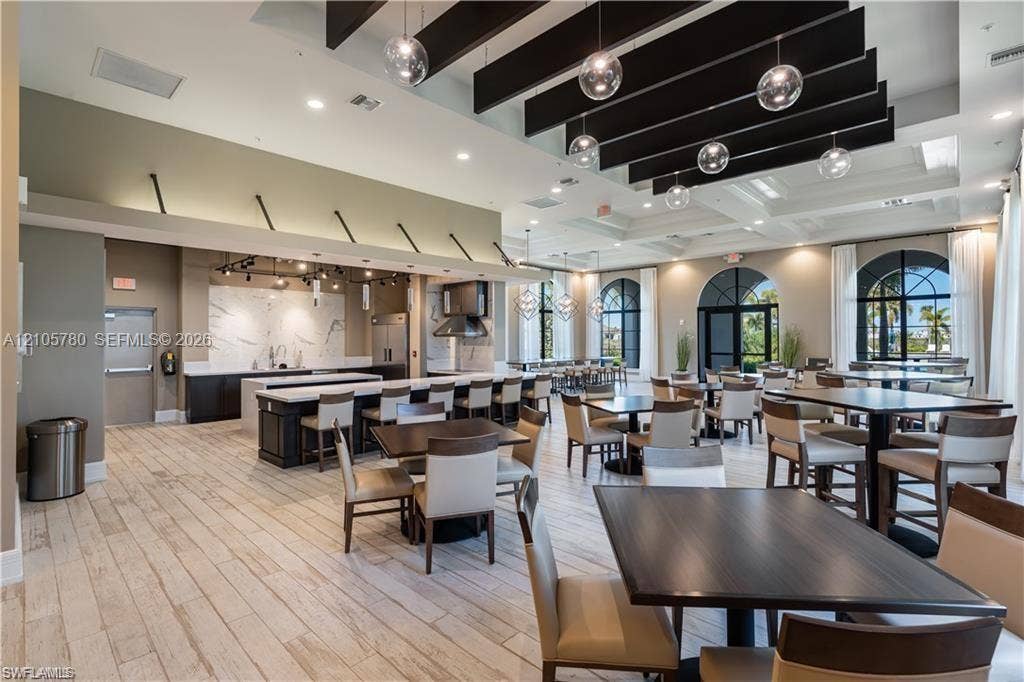 Expansive interior space featuring wood-finish flooring, a coffered ceiling with suspended black structural beams, integrated globe pendant lighting, and arched window frames