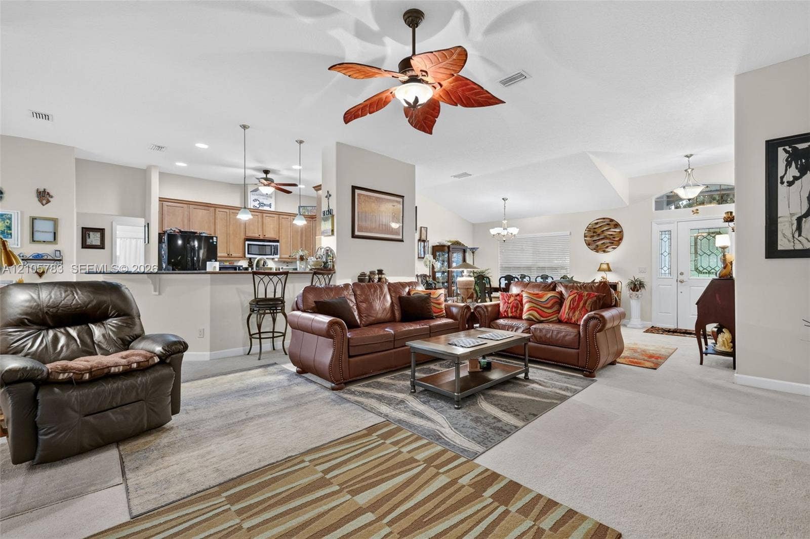 Open-concept interior featuring vaulted ceilings, recessed lighting, a kitchen breakfast bar, and decorative ceiling fan fixtures