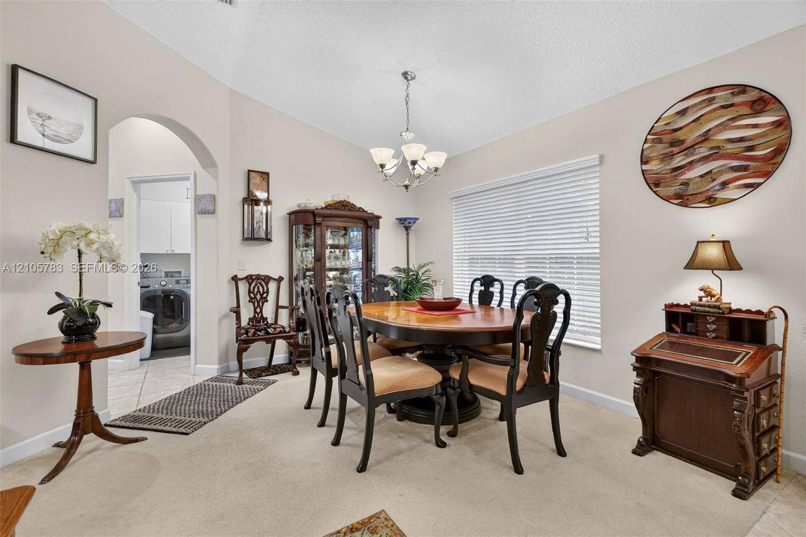 Dining area featuring vaulted ceilings, arched entryway, multi-arm chandelier, and large window with blinds